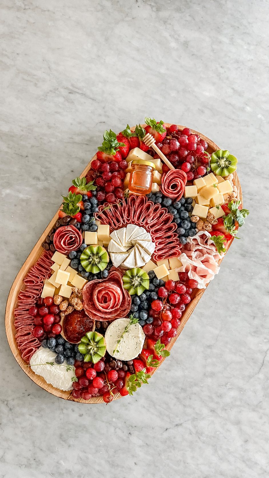 Oval charcuterie board arranged with berries, cheese and meat roses